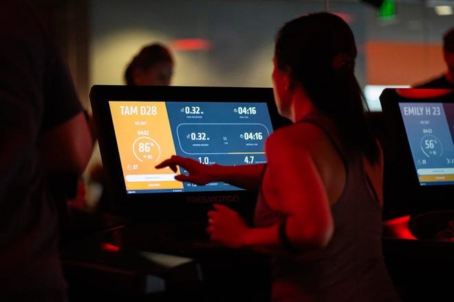 A runner looks over her data displayed on a treadmill as people work out during the noon hour at Orange Theory Fitness in Edina, Minnesota.